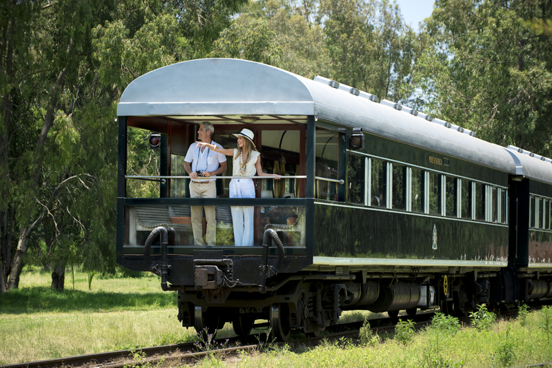 Travellers on the open observation balcony at the rear of the Rovos Rail Pride of Africa, watching the landscape pass.